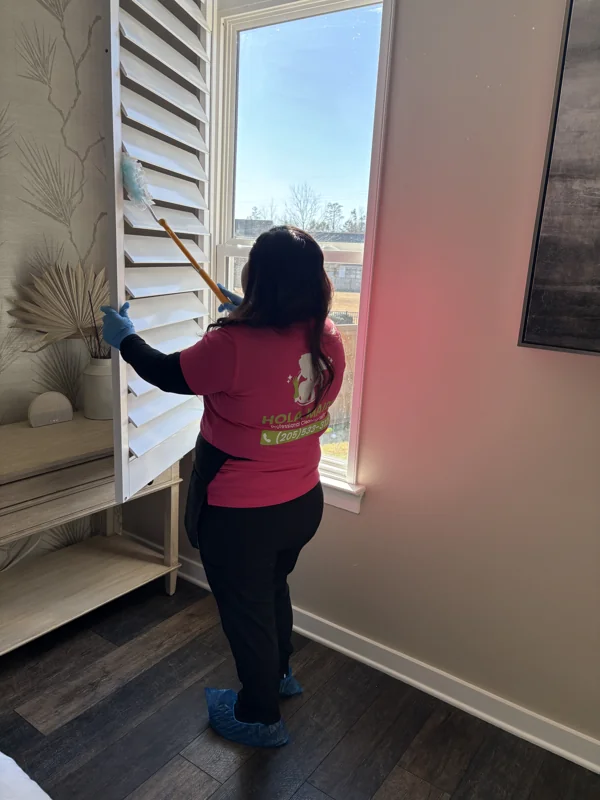 A Hola Maids team member carefully dusting white window shutters
